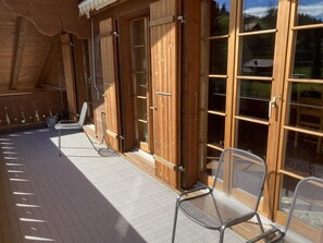 A wooden deck with a covered area, a metal chair, and a sliding glass door. - Fichte (Sulliger) Appartement/Fewo, Dusche oder Bad, WC 6-Bettwohnung by Interhome (Gstaad)