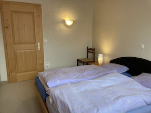 A bedroom with two beds, a wooden door, a chair, and a wall-mounted light fixture.