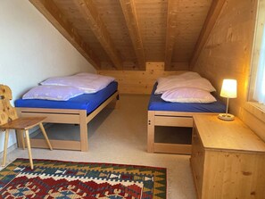 A small, cozy attic bedroom with two wooden bunk beds, a small wooden chair, a nightstand with a lamp, and a colorful rug. - Fichte (Sulliger) Appartement/Fewo, Dusche oder Bad, WC 6-Bettwohnung by Interhome (Gstaad)