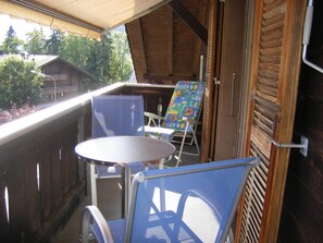 A balcony with a table and two chairs, a wooden deck, and a view of trees and buildings. - Arlette Nr. 30 Appartement/Fewo, Dusche oder Bad, WC 2-Bettwohnung by Interhome (Gstaad)