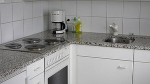 Una cocina con armarios blancos, horno empotrado, cafetera y un lavamanos.