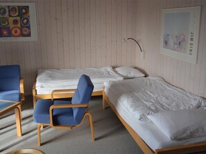 A room with two single beds, a blue chair, and a wooden table. - Arlette Nr. 30 Appartement/Fewo, Dusche oder Bad, WC 2-Bettwohnung by Interhome (Gstaad)
