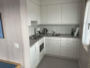 A compact kitchen with white cabinets, a built-in oven, a coffee maker, and a kettle. - Arlette Nr. 30 Appartement/Fewo, Dusche oder Bad, WC 2-Bettwohnung by Interhome (Gstaad)