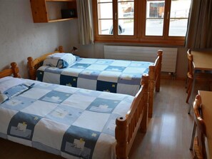 Een kamer met twee houten bedden, een tafeltje en een raam met gordijnen.