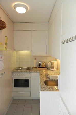 Cocina compacta con gabinetes blancos, horno empotrado, estufa a gas, tostadora y fregadero.