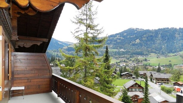 Un balcon en bois offrant une vue sur un village et des montagnes.
