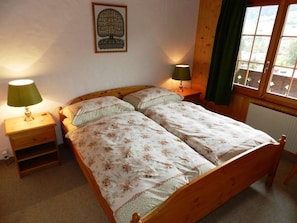 Un lit double avec une literie à motifs floraux, deux tables de chevet avec des lampes, un tableau encadré au mur et une fenêtre avec des rideaux.