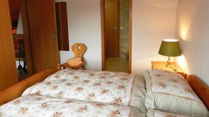 Une chambre à coucher comprenant un lit, une chaise, une table de chevet avec une lampe et une porte donnant sur une autre pièce.