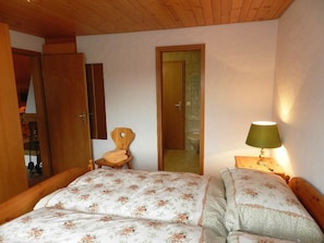 A bedroom with a bed, a chair, a nightstand with a lamp, and a door leading to another room. - Hornflue (Baumann) Appartement/Fewo, Dusche oder Bad, WC 4-Bettwohnung by Interhome (Gstaad)