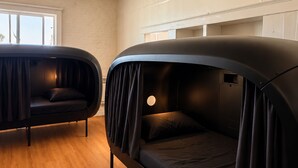A modern room with two black, curved beds with curtains, a wooden floor, and a window with natural light.