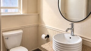 A bathroom with a toilet, a sink, a mirror, and a window.