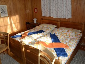 Ein Zimmer mit Holzboden, zwei Betten, einem Stuhl, einem Schreibtisch und einem Fenster mit Vorhängen.