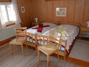 Een kamer met houten lambrisering, een bed, twee stoelen, een radiator en een raam met gordijnen.