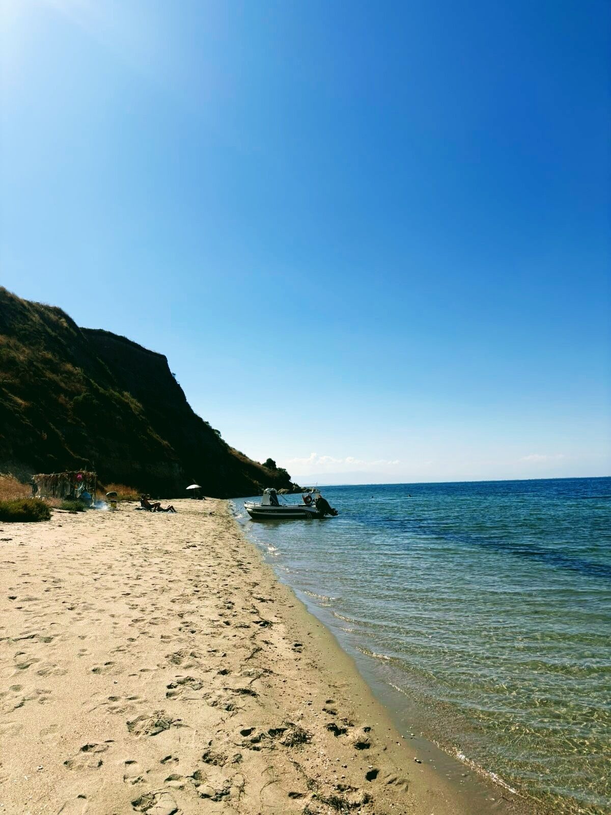 A beach with a boat near the shore, clear skies, and a hilly landscape in the background.