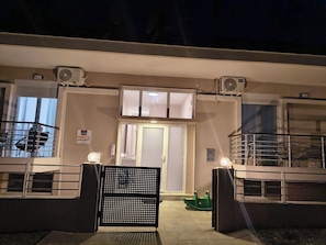 Entrada de un edificio con un camino de acceso porticado, un cartel que indica 'Apartments' y dos unidades de aire acondicionado instaladas en la pared.