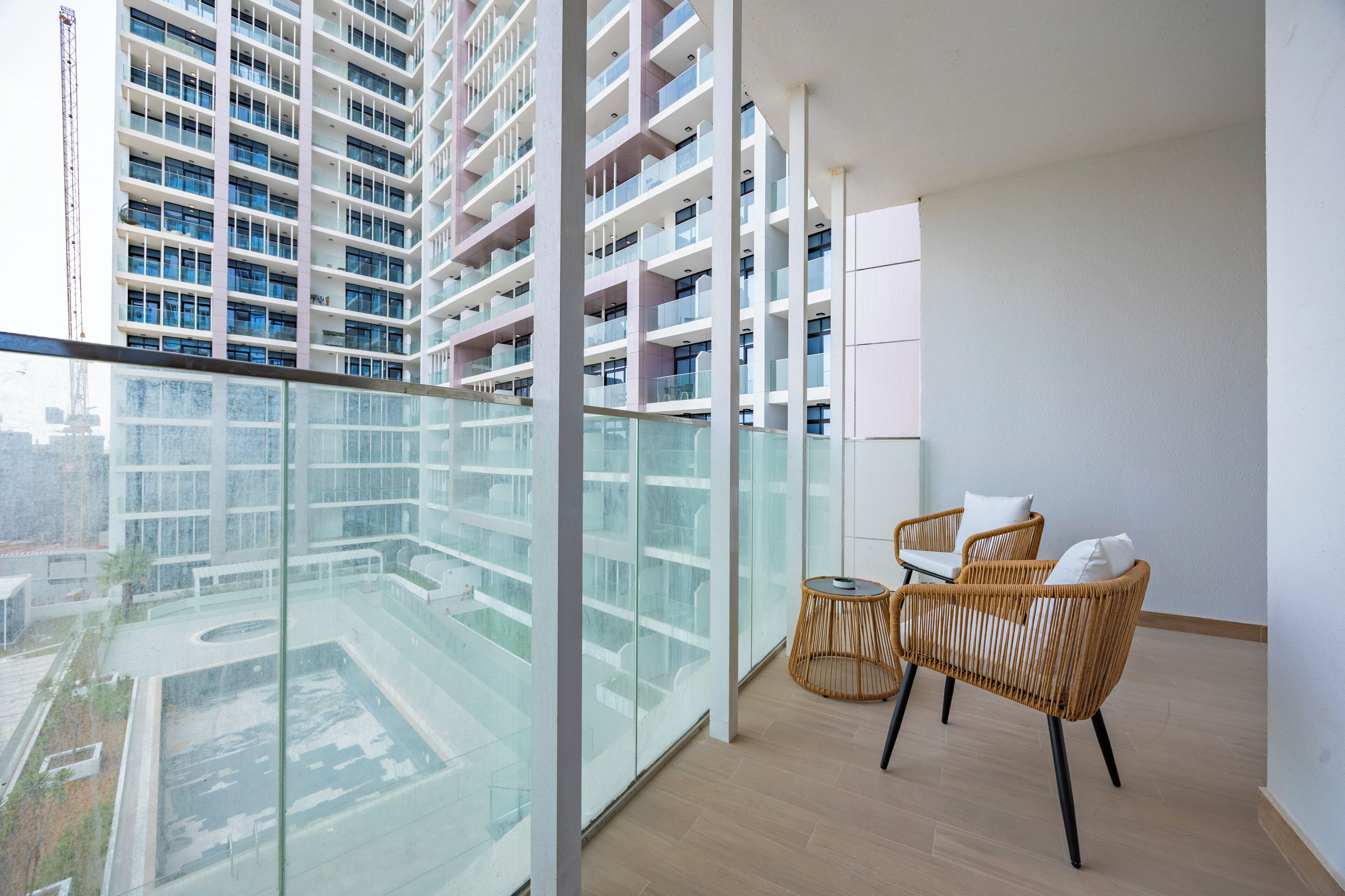 Ein Balkon mit Glasgeländer, zwei Korbstühle und Blick auf ein Hochhaus.