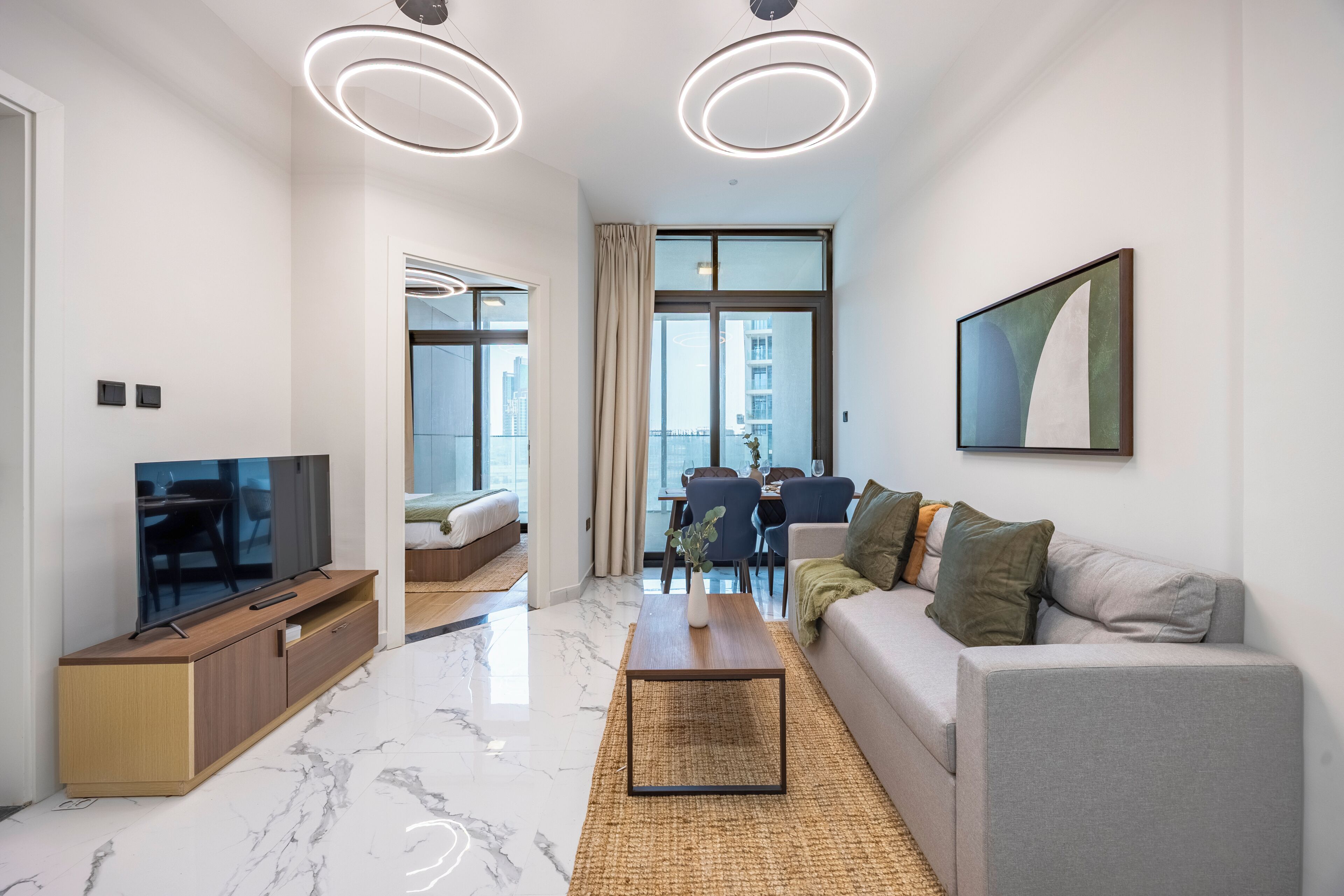 A modern living room with a flat-screen TV, a sofa, a coffee table, and a dining area with a table and chairs.