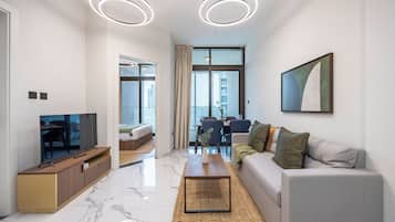 A modern living room with a flat-screen TV, a sofa, a coffee table, and a dining area with a table and chairs.