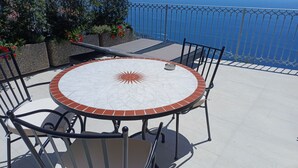 Une table ronde d’extérieur ornée d’un motif solaire, entourée de chaises, installée sur une terrasse offrant une vue sur la mer.