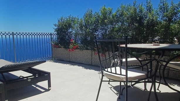 Une terrasse extérieure avec une table et des chaises, une clôture bleue et de la verdure en arrière-plan.