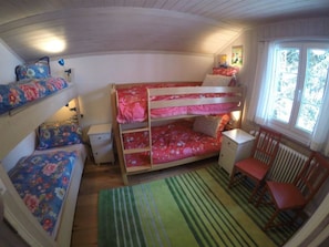 Ein Schlafsaalzimmer mit Etagenbett, Fenster, Stuhl und Heizkörper.