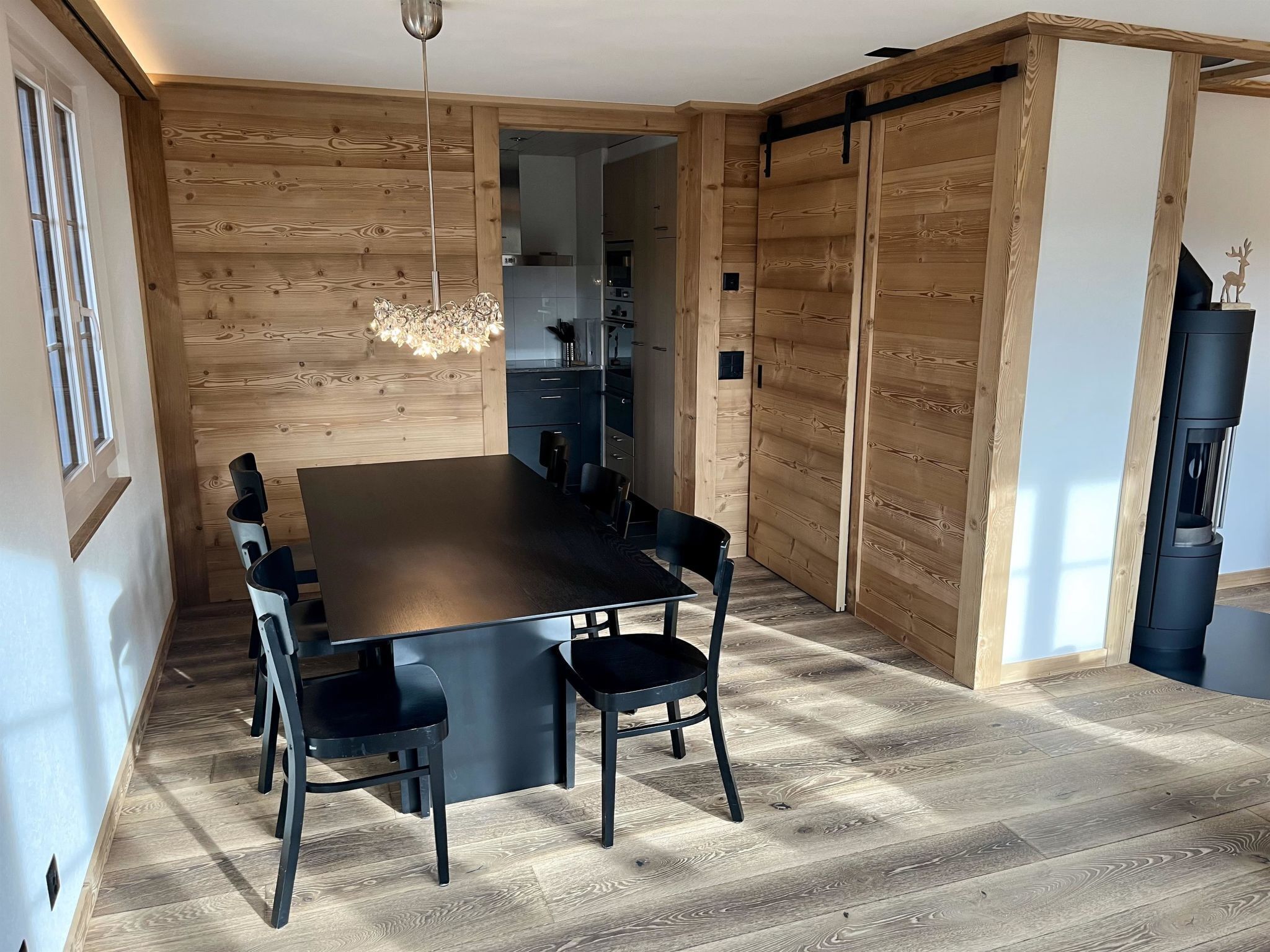 A modern dining area with a wooden wall, a black dining table, and chairs.