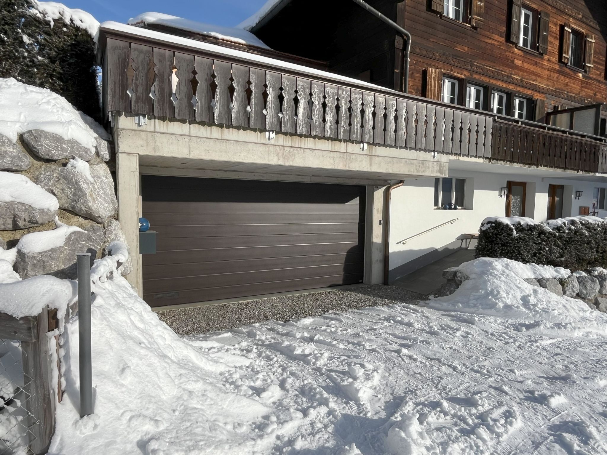 Un immeuble résidentiel doté d’un garage, de murs en pierre et recouvert de neige.