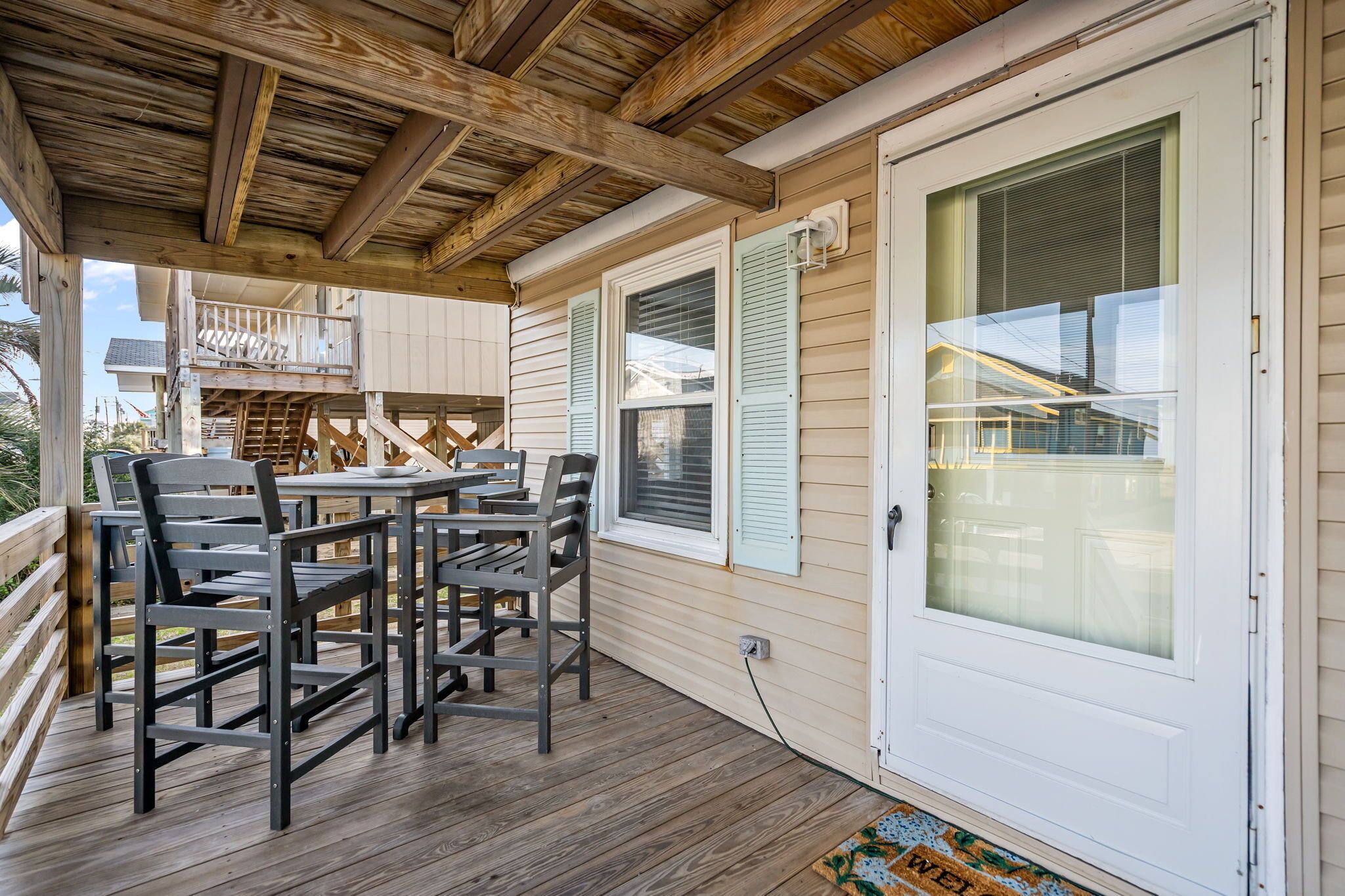 A covered outdoor area with a table and chairs, a wooden deck, and a white door with a window.