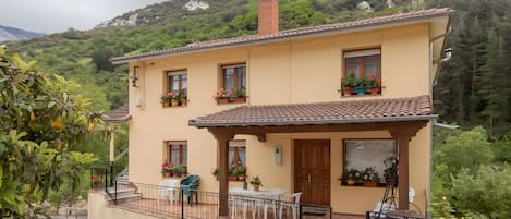 A two-story house with a balcony, potted plants, and a view of a mountainous landscape.
