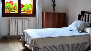 A bedroom with a bed, a dresser, a radiator, and a window with potted plants.