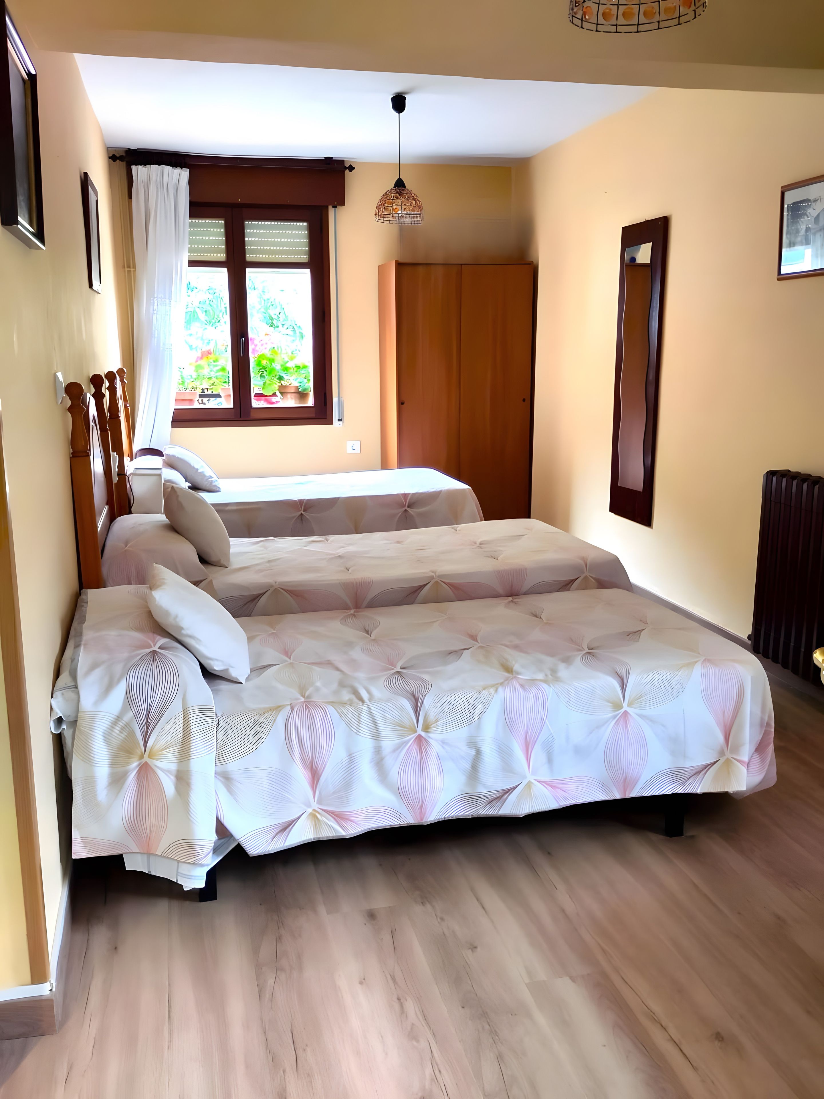 Un dormitorio con dos camas, una ventana con cortinas, una lámpara colgante y un radiador.