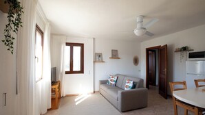 A living room with a sofa, a TV, a ceiling fan, and a dining area with chairs and a table. - Casa del Miso by Wonderful Italy (Sardegna)