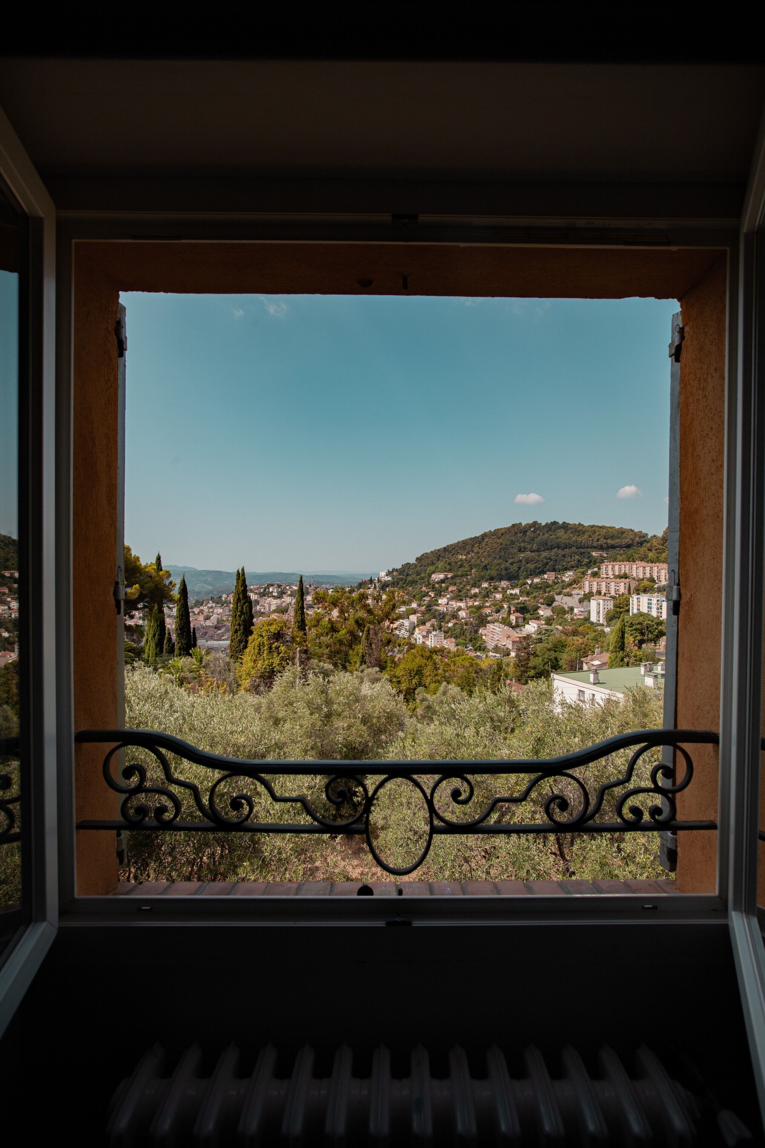 A balcony with a wrought iron railing overlooking a residential area with houses and trees.