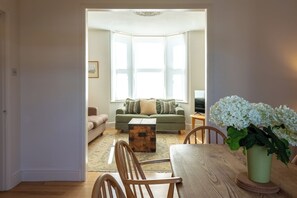 A living room with a sofa, a coffee table, and a wooden dining table. - Charming Garden Home in Brixton (Greater London)