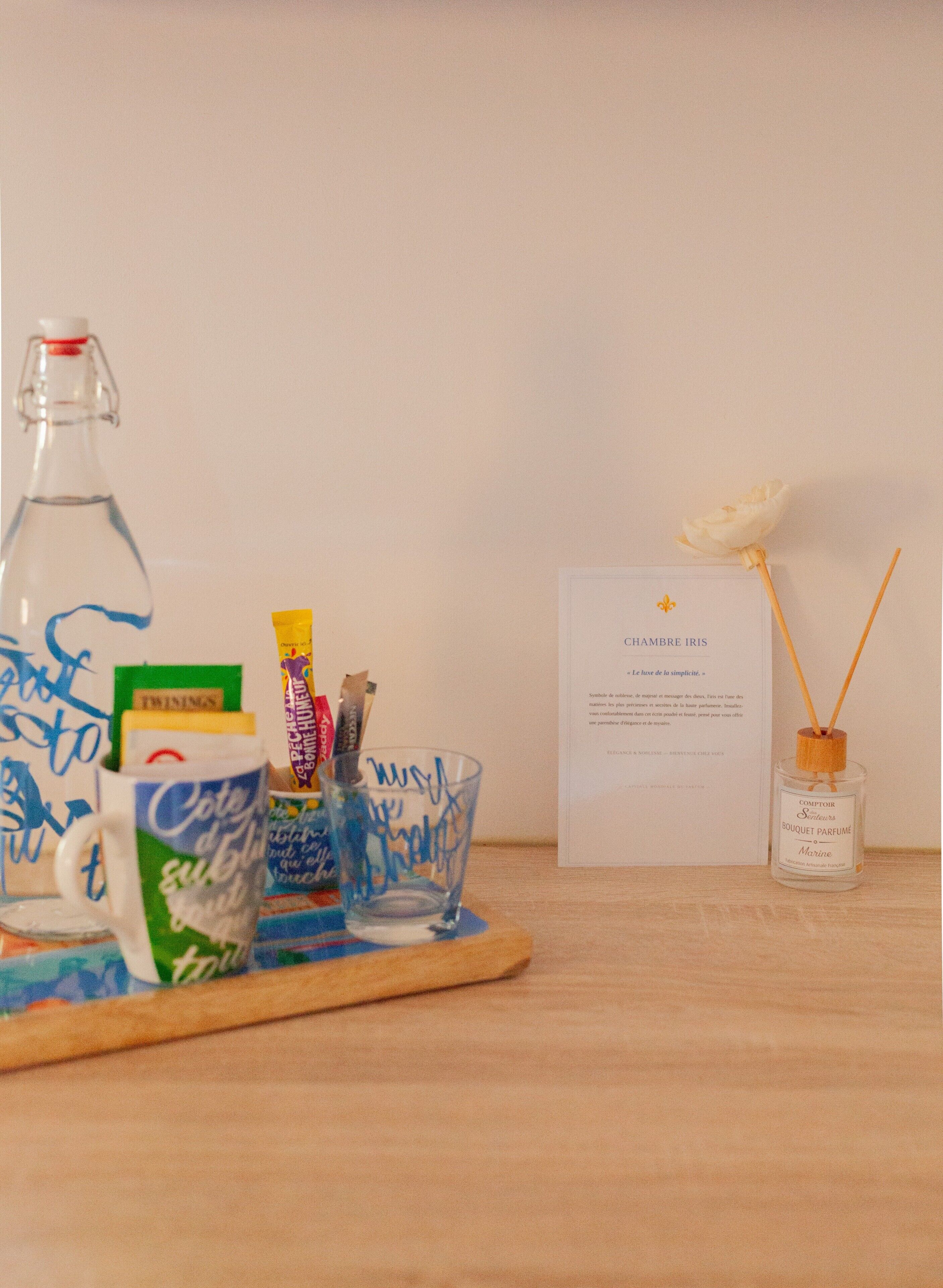 A table with a bottle, a glass, a mug, a card, and a perfume bottle.