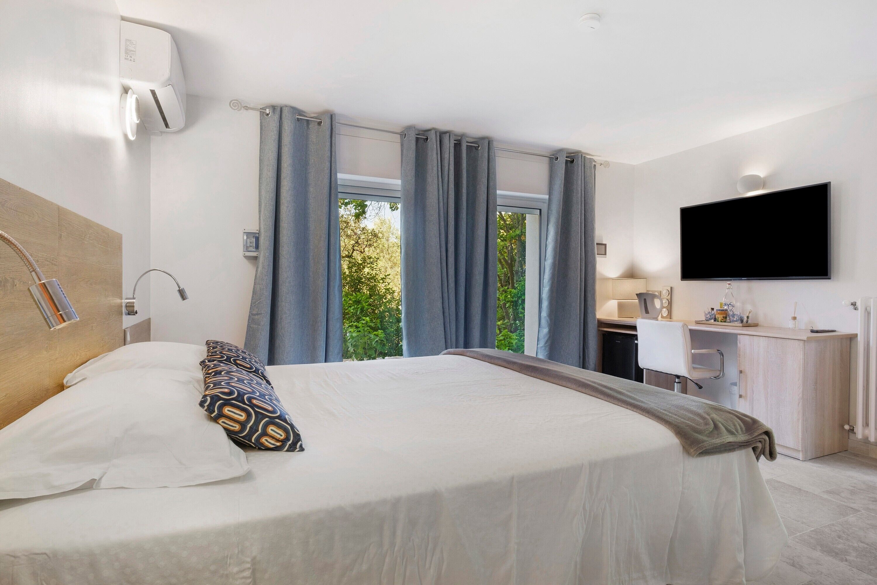 A hotel room with a bed, a desk, a TV, and a window with curtains.