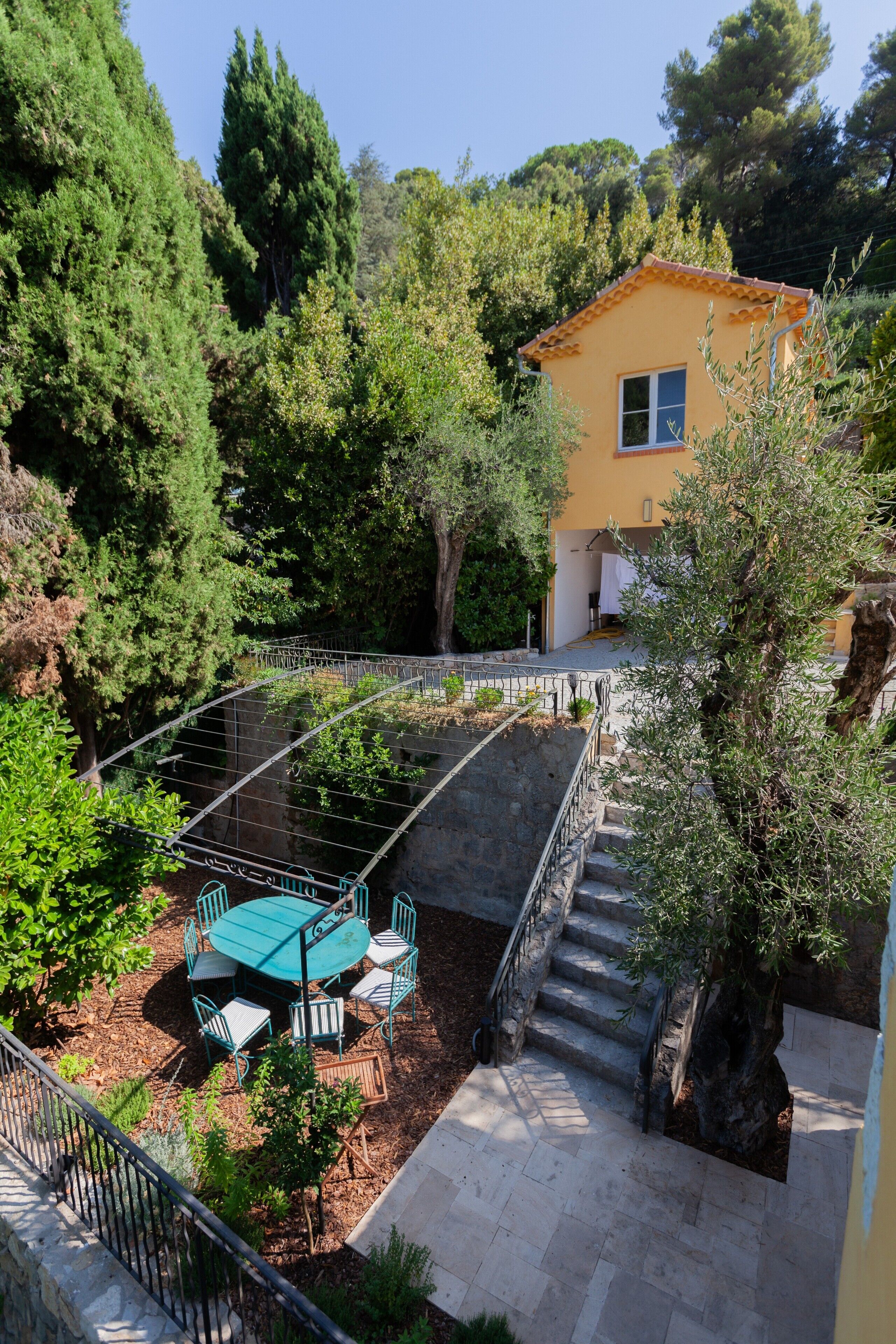 Une cour avec une table et des chaises, un escalier et un bâtiment à la façade jaune.