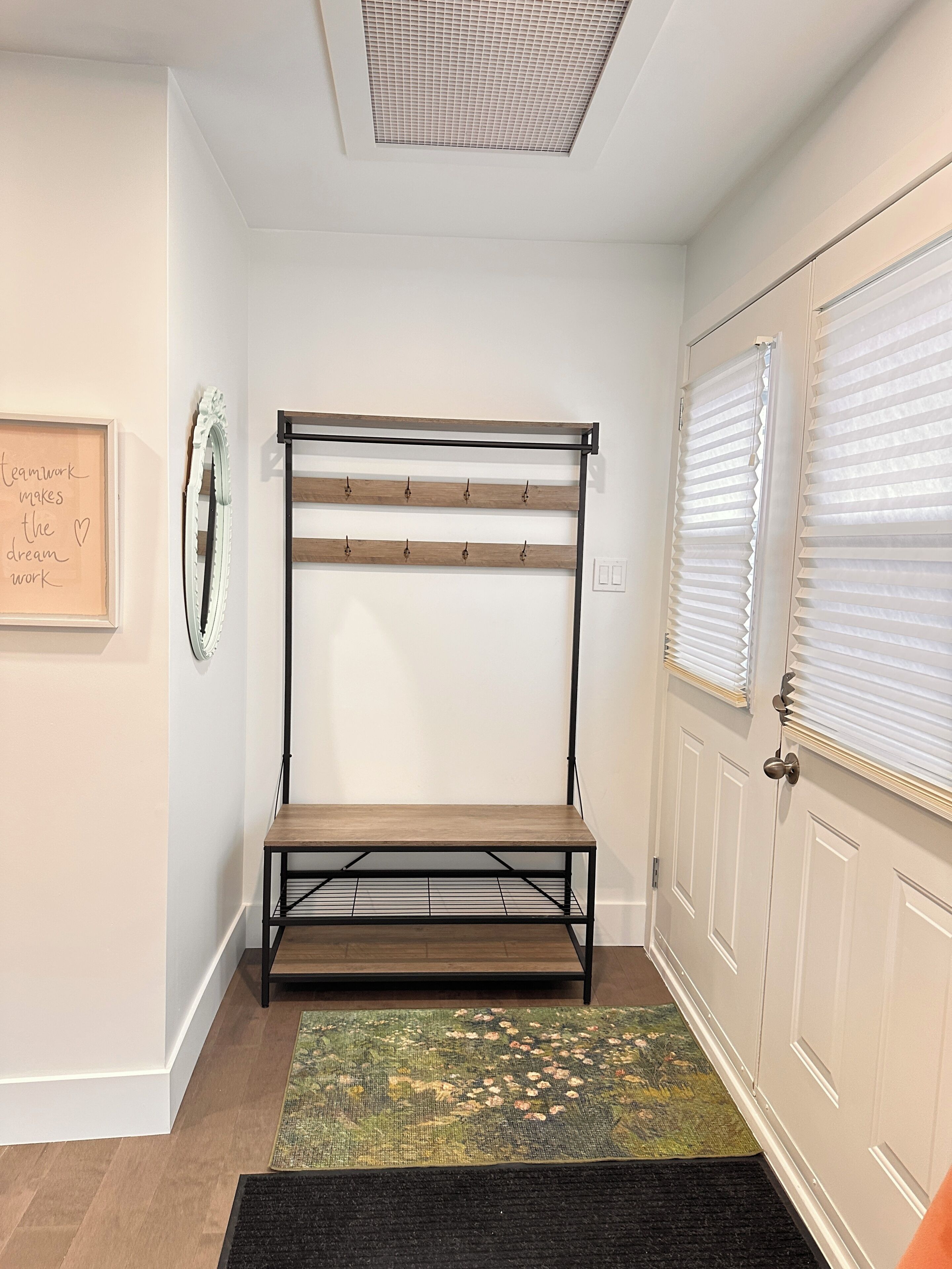 Une chambre avec un lit superposé, un porte-manteau fixé au mur, une citation inspirante encadrée, une porte avec des stores et un tapis à motifs.