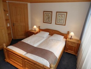 A wooden four-poster bed with white linens, two bedside tables with lamps, and two framed botanical prints on the wall. - Lisa Appartement/Fewo, Dusche oder Bad, WC 4-Bettwohnung by Interhome (Gstaad)
