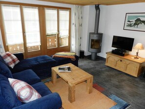 A cozy living room with a sofa, a television, a wooden cabinet, and a fireplace. - Lisa Appartement/Fewo, Dusche oder Bad, WC 4-Bettwohnung by Interhome (Gstaad)