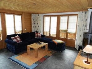 Een gezellige woonkamer met een donkerblauwe bank, een houten salontafel en een open haard.