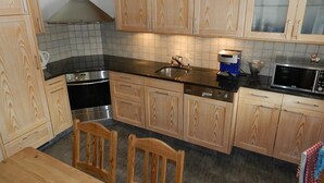 Uma cozinha com armários de madeira, bancada preta, pia de aço inoxidável, micro-ondas e máquina de café.