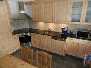 A kitchen with wooden cabinets, a black countertop, a stainless steel sink, a microwave, and a coffee maker. - Lisa Appartement/Fewo, Dusche oder Bad, WC 4-Bettwohnung by Interhome (Gstaad)