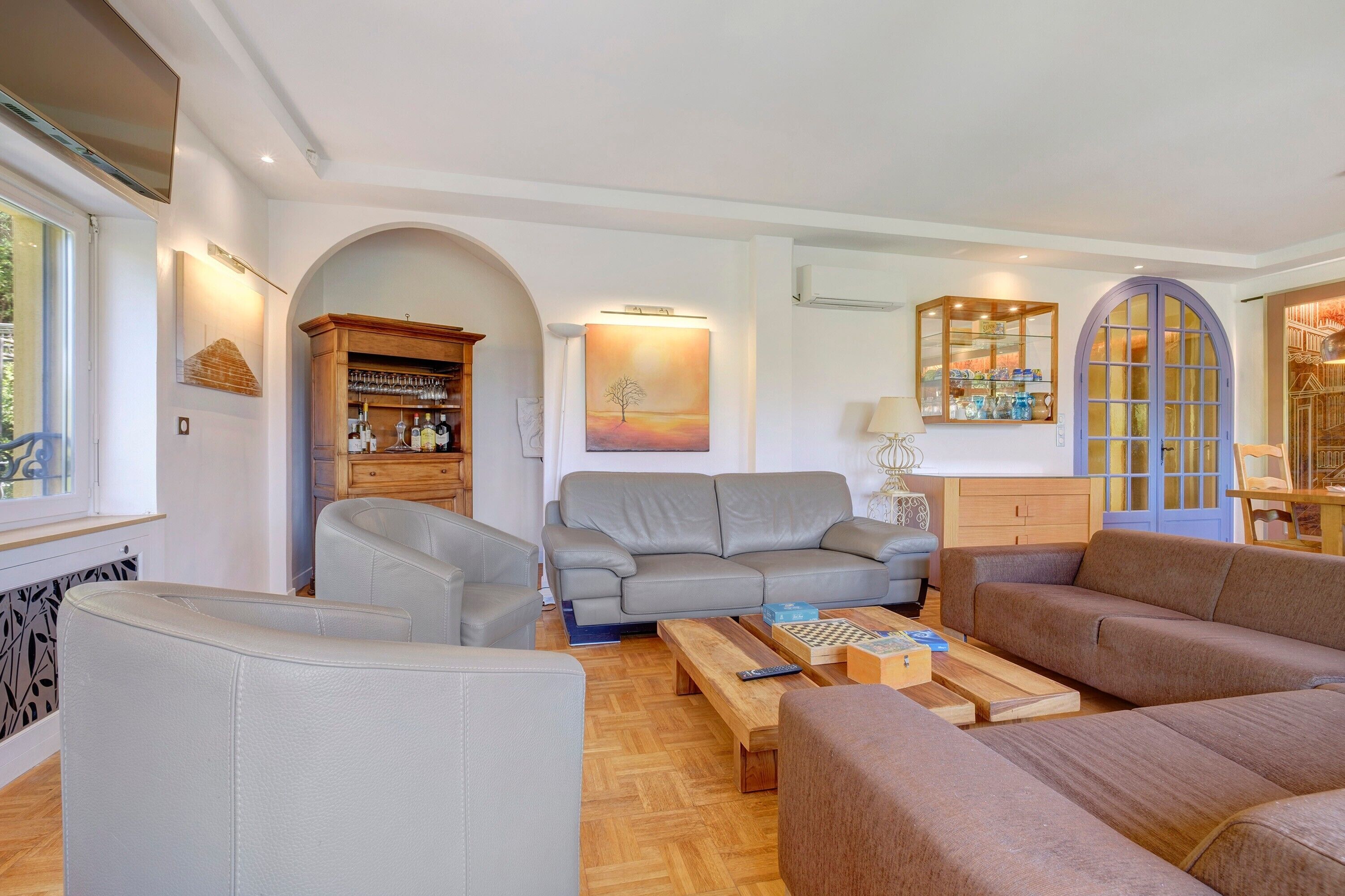 Sala de estar com sofá cinza, mesa de centro de madeira e aparador com copos.
