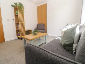 A living room with a grey sofa, a wooden coffee table, a grey armchair, a bookshelf with plants, and a wooden wardrobe.