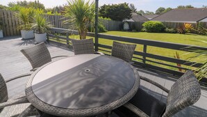 A covered patio with a round table and wicker chairs, overlooking a grassy yard and a wooden fence. - Agan Paradhis (Newquay)