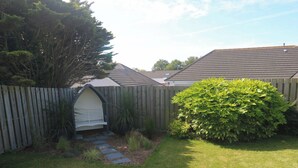 A backyard with a wooden fence, a small garden with stepping stones, and a large bush. - Agan Paradhis (Newquay)