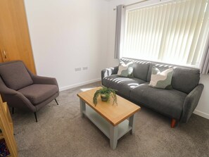 Una sala de estar con un sofá gris, un sillón marrón y una mesa de centro de madera con una planta.