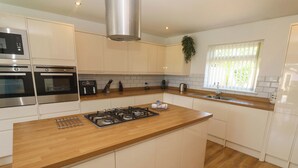 A modern kitchen with built-in appliances, a central island, and a window with blinds. - Agan Paradhis (Newquay)
