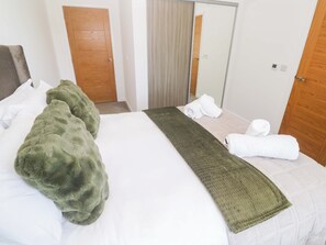 Una habitación de hotel con una cama, un plaid verde, toallas blancas, un espejo y puertas de madera.